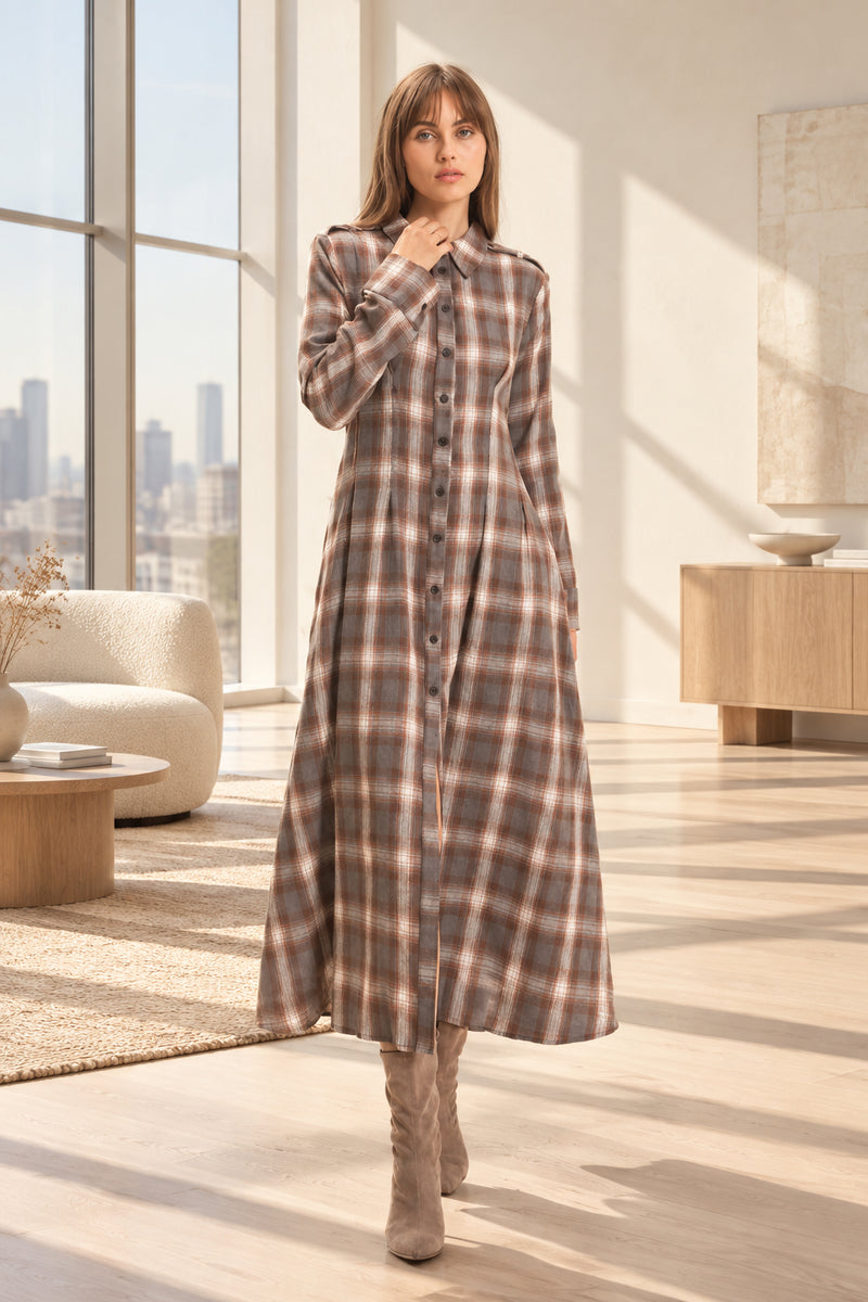 A woman modeling a long-sleeve, button-front midi dress with a brown, beige, and white plaid pattern, paired with brown boots, set against a plain light beige studio background.