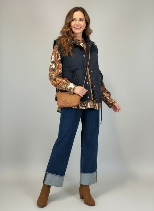 Mannequin wearing a navy puffer vest over a patterned shirt with blue jeans on a plain background