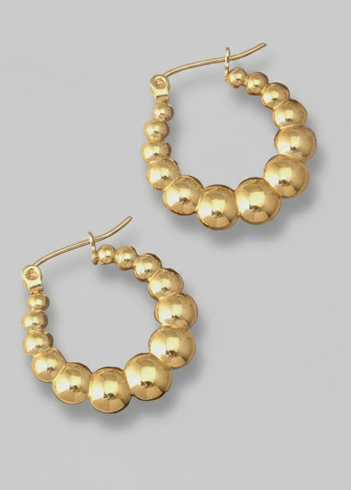 Gold hoop earrings with bead detailing on a wooden stand against a neutral background