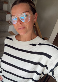 A person wearing a white ribbed knit sweater with black horizontal stripes, photographed indoors near a staircase. The image is upside down, and the person is also upside down relative to the frame.