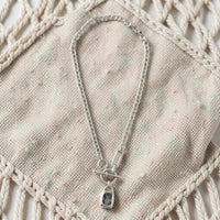 Chandeliers Boutique ny pewter toggle necklace with a silver-tone chain and a dark rectangular pendant on fabric.