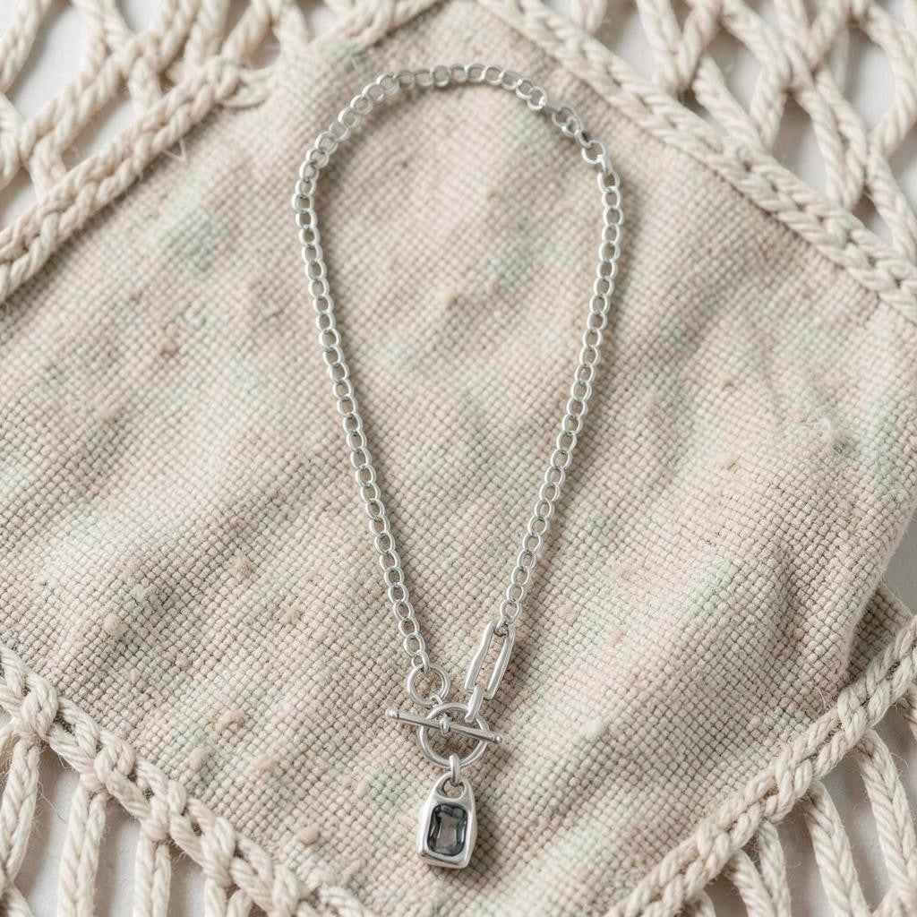Chandeliers Boutique ny pewter toggle necklace with a silver-tone chain and a dark rectangular pendant on fabric.