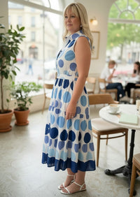 Woman wearing a Chandeliers Boutique ny sleeveless cotton polka dot midi dress with a collared neck and belted waist.