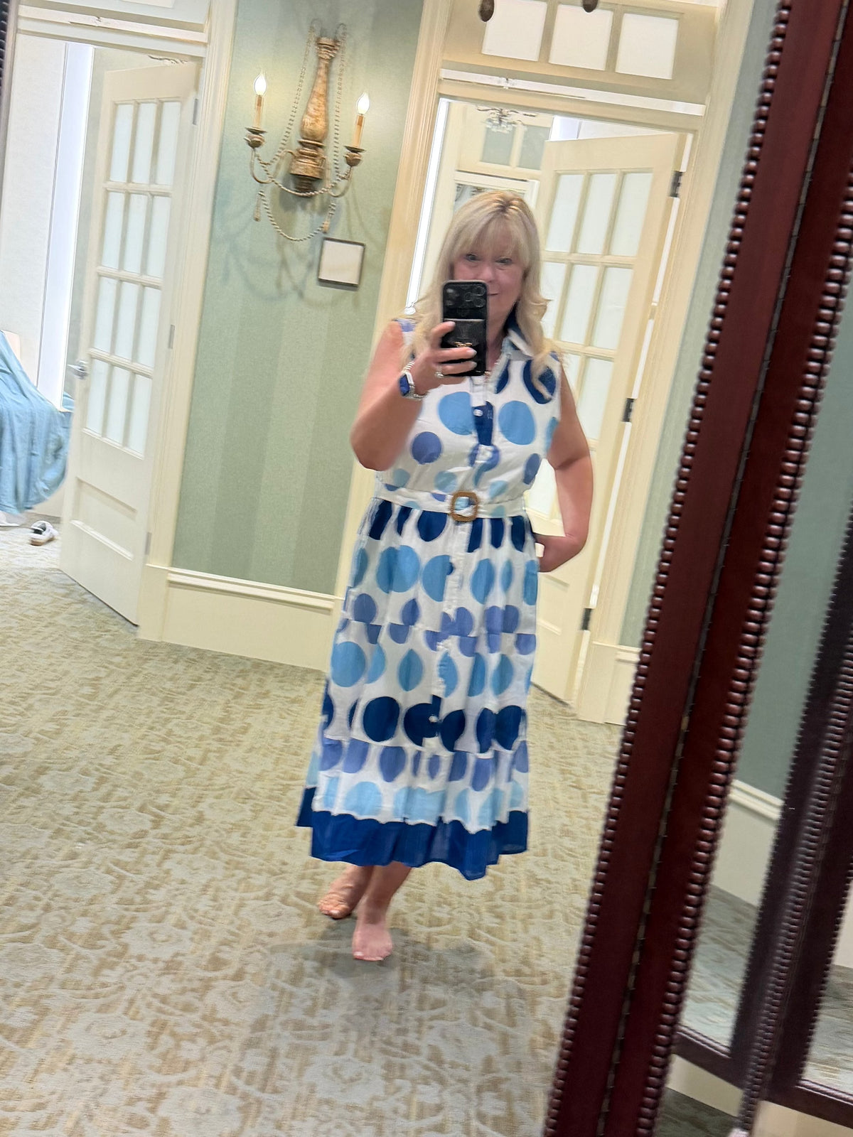Woman wearing a Chandeliers Boutique ny sleeveless cotton polka dot midi dress with a collared neck and belted waist.